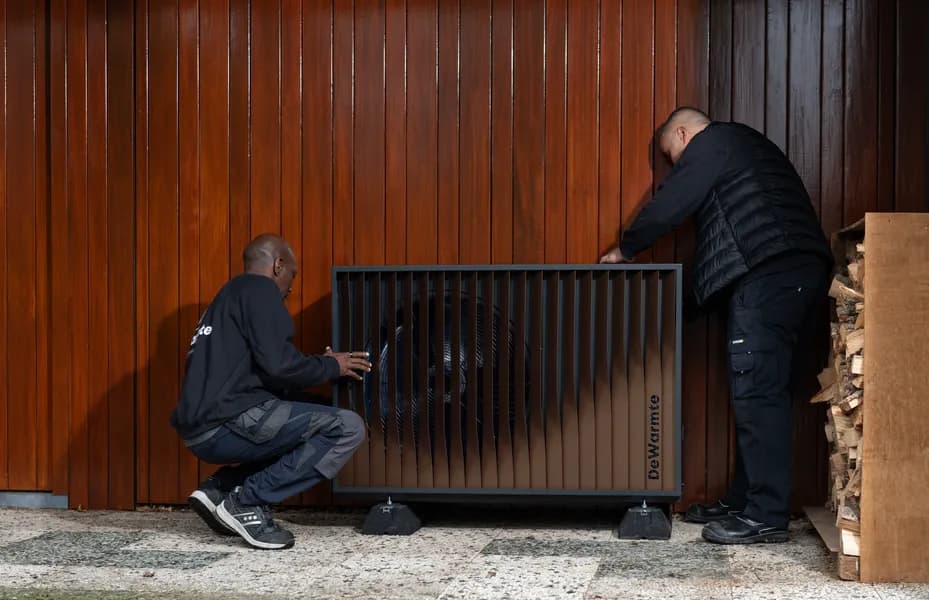 Buitenunit van een warmtepomp naast een tussenwoning met tuin